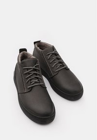 Scarpe in pelle nera con una texture liscia, punta arrotondata e suola in gomma leggera. Presentano lacci grigi e accenti di cucitura.