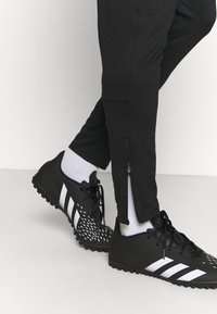 Zwarte sportbroek met ritsmanchetten, in combinatie met zwart-witte voetbalschoenen met een gestructureerde bovenkant en een gemusterd design.