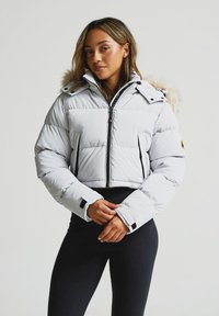 Gari kājāds jaka gaiši pelēkā krāsā ar mākslīgā pūka kapuci, melno rāvējslēdzēju, sānu kabatām un regulējamām aprocēm. Gluda tekstūra, silts dizains.