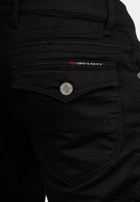 Jeans in denim neri a vestibilità slim, con logo sulla tasca posteriore, hardware argentato e dettagli di cucitura discreti per un tocco di texture.