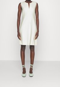 Robe sans manches vert menthe avec un décolleté en V, une texture lisse et une coupe ajustée, associée à des ballerines à nouer à la cheville de couleur vert menthe clair.