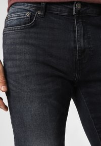 Jeanși din denim de un albastru închis, cu croi slim. Caracteristici includ închidere cu buton, design cu cinci buzunare și o textură subtilă cu ușoare decolorări.