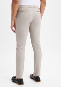 Pantaloni beige slim-fit realizzati in un tessuto morbido. Presentano tasche posteriori con una ricamata discreta e una vita aderente.