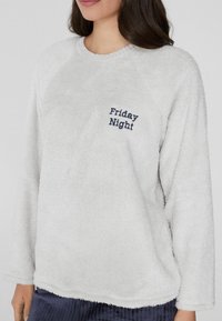 Sudadera de forro polar gris claro con una textura suave, que presenta el texto "Friday Night" bordado en azul oscuro en el pecho. Cuello redondo.