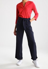 Chemise rouge à manches longues avec un col boutonné, associée à un pantalon large à rayures marines et des baskets blanches. Tissu lisse avec une coupe décontractée.