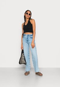 Top cropped preto, jeans de cintura alta azul claro, sandálias de padrão de leopardo e uma bolsa de malha preta. Os acessórios incluem óculos de sol redondos.