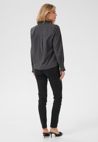 Grijze blouse met een gerimpelde halslijn, rugplooidetail, gecombineerd met zwarte skinny jeans en zwarte hakken.