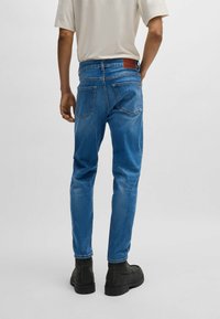 Modré denimové džíny so strihom rovného nohu, koženým štítkom na zadu a dvoma zadnými vreckami. Tkanina sa javí hladká s klasickým vzhľadom.