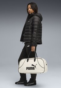 Giacca a vento nera, pantaloni della tuta neri e scarpe nere. Borsone bianco con logo Puma nero. Materiale liscio con texture distintive.