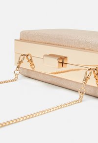 Kovový psaníčko ve zlatém odstínu s texturovaným, světlým zlatým tělem, obdélníkovým tvarem a řetízkovým popruhem. Obsahuje jednoduché uzavírání na klip.