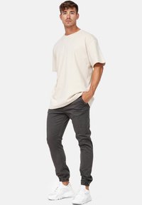 Camiseta de gran tamaño beige, fabricada en un algodón ligero. Pantalones en gris oscuro con corte tapered, material elástico y puños elásticos. Zapatillas blancas con detalles de malla.