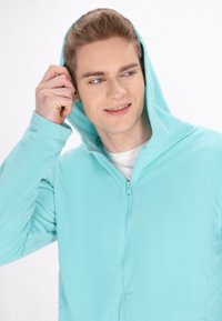Világoskék, cipzáros kapucnis pulóver bolyhos anyagból, elöl cipzárral, kapucnival és texturált szövettel.