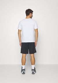 Fehér, rövid ujjú póló, fekete sorttal párosítva. Az öltözék lazán illeszkedik, a kényelem és a hétköznapi viselet érdekében tervezve.