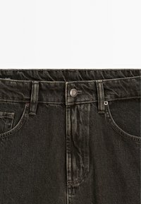 Jean en denim gris foncé au niveau de la taille avec un bouton en métal, des passants de ceinture et des coutures visibles sur les poches et les coutures.