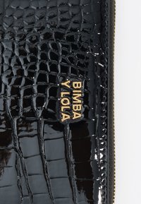 Bolsa de mano negra brillante con un patrón de cocodrilo, con el nombre de la marca "BIMBA Y LOLA" en letras doradas en el frente.