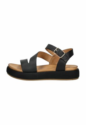 Sandalias de cuero negras con diseño de tiras cruzadas, hebilla ajustable y suela gruesa negra. La plantilla de color marrón claro añade contraste.