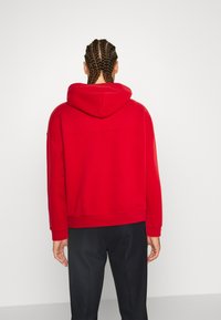 Czerwona bluza z kapturem o luźnym kroju, z ribbowanymi mankietami i dołem. Gładki materiał, jednolity wzór, bez widocznych wzorów ani logo.