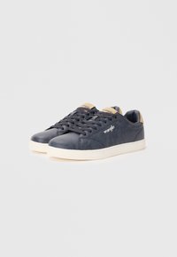 Baskets en cuir bleu marine avec une texture lisse, semelle en caoutchouc blanche et accents crème. Présente des côtés perforés et un logo contrastant.