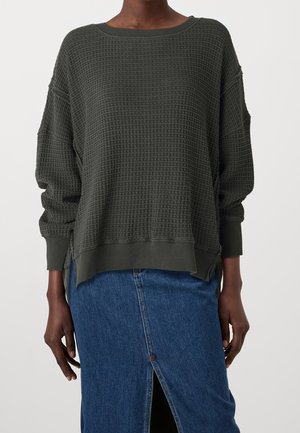 Dark green waffle-knit long-sleeve sweater with ribbed cuffs and hem worn with a blue denim skirt featuring a front slit.