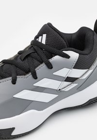 Chaussure de sport noire et grise avec tige en maille, superpositions synthétiques, bandes blanches en accent et semelle extérieure en caoutchouc texturé.