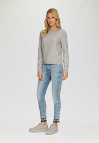 Grijze trui, aansluitend ontwerp, katoenen stof; gecombineerd met lichtblauwe skinny jeans en grijze sneakers. Eenvoudige, nette lijnen zonder opvallende patronen.