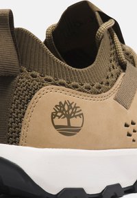 Brun sneaker med en texturerad, vävd ovandel, suède detaljer och en vit sula. Har en trälogotyp och förstärkt hälflik.