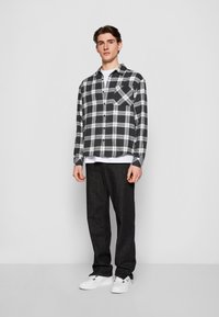 Sort og hvidternet flannel skjorte med lange ærmer, knaplukning foran og en enkelt brystlomme, parret med mørke jeans og hvide sneakers.