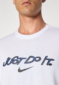 White cotton t-shirt featuring a blue and black "Just Do It" print and a black Nike logo positioned centrally on the chest.