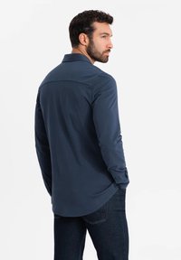 Marineblauw overhemd met lange mouwen en een kraag, zachte textuur en gefixeerde manchetten, met een gebogen zoom en een platte yoke over de rug.