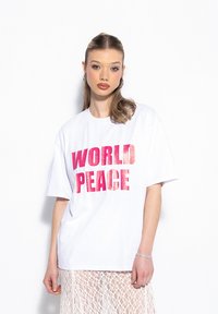 Biała, oversize koszulka z odważnym, różowym napisem "ŚWIATOWY POKÓJ". Wykonana z bawełny, z krótkimi rękawami i luźnym krojem. Noszona z koronkową spódnicą.