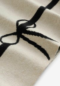 Tekstiil kreemika taustaga, millel on silmapaistev must vibu kujundus. Pehme tekstuur, kootud kangas nähtavate kiudude ja mustritega.