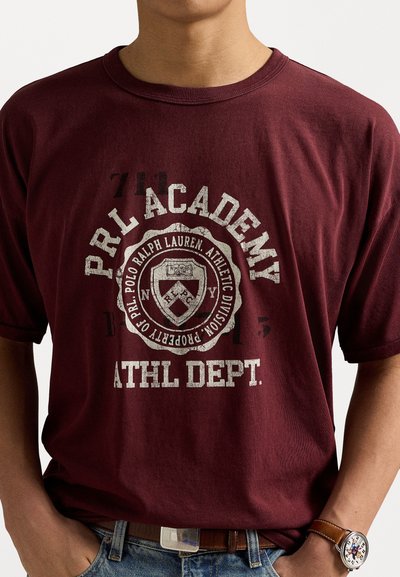 Bordeaux katoenen T-shirt met een vintage-stijl graphic met een schild, "PRL ACADEMY," en "ATHL DEPT." in versleten wit gedrukt.