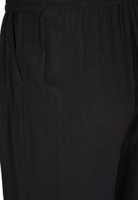 Pantalons en tissu plissé noir avec une surface texturée, dotés de poches latérales et d'une taille élastique pour plus de confort.