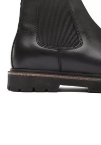 Stivaletto in pelle nera con pannello laterale elastico a coste, punta rotonda e suola in gomma resistente con scanalature testurizzate.