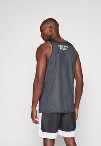 Top sin mangas de baloncesto de malla negra con el texto "Chicago Bulls" en la parte posterior, combinado con pantalones cortos de malla en blanco y negro.