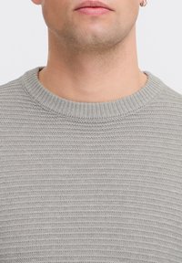 Gray knitted sweater featuring a ribbed round neckline and a textured pattern throughout. Close-up view emphasizing fabric detail.