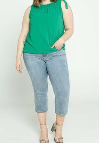 Top verde senza maniche con scollo arricciato e lacci laterali, abbinato a jeans blu chiaro a vita corta e sandali con tacco verdi.