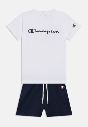 Maglietta bianca a maniche corte Champion con logo nero sul petto e sulla manica, abbinata a pantaloncini blu scuro con coulisse bianca e piccolo logo.