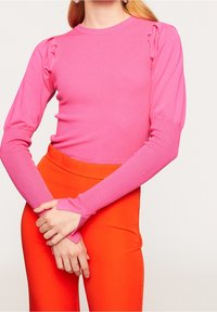 Pull à manches longues rose côtelé avec détail froncé à l'épaule, assorti à un pantalon orange ajusté. Le tissu semble lisse et élastique.