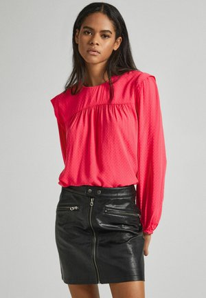 Blusa rosa brillante a maniche lunghe con finitura testurizzata e dettagli arricciati, abbinata a una mini gonna in pelle nera con tasche con zip.