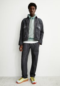 Donkergrijze spijkerjas en -broek met daaronder een mintgroene hoodie. De schoenen hebben een gele basis en rode accenten, met zwarte veters.