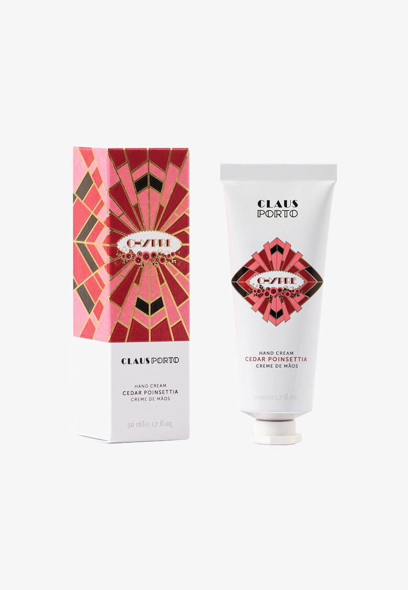 Handcreme in einer weißen Tube mit einer dekorativen rosa-roten geometrischen Verpackung mit goldenen Akzenten. Auf dem Produkt steht "Cedar Poinsettia".