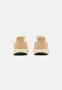 Baskets en daim tan et en cuir crème avec une semelle en caoutchouc texturée, dotées d'un col rembourré et d'un design minimaliste.