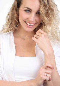 Silver necklace with a minimal design, paired with rings. Model wears a white shirt and tank top, displaying light skin and wavy hair.
