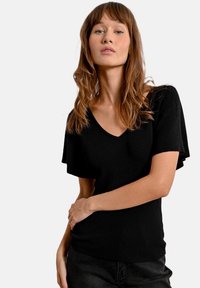 Top nero a coste con scollatura a V e maniche corte a sbuffo, caratterizzato da una silhouette aderente e una texture liscia.