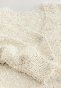Light beige cardigan made of fluffy, textured yarn. Features a deep neckline and metallic buttons along the front. Soft, warm fabric.