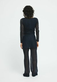 Navyblå, långärmad spetsdräkt med en figurnära topp och flödande byxor, som visar ett diamantmönster och genomskinlig textur.