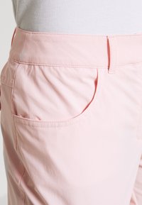 Ljust rosa byxor med en mjuk textur, standard midjeband, sidofickor och subtila sömnadsdetaljer.