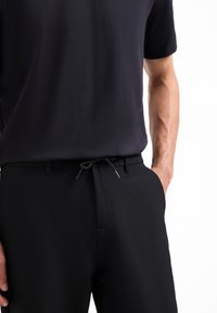 Zwart shirt met korte mouwen gecombineerd met zwarte broeken met een trekkoord in de taille. Glad materiaal met een strak, minimalistisch ontwerp.