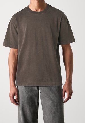 Dunkelgraues T-Shirt mit kurzen Ärmeln aus weicher Baumwolle. Lässige Passform mit rundem Ausschnitt und minimalen Nähten.